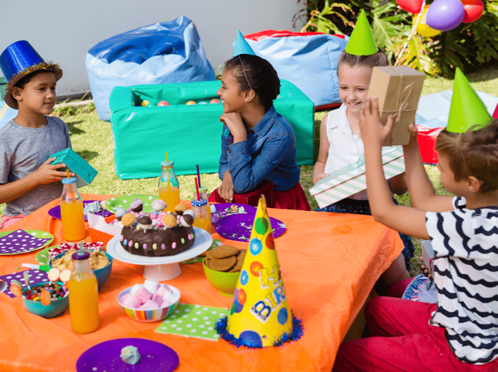 Kids enjoying an outdoor birthday party with colorful decorations, gift exchange, and a chocolate cake centerpiece.