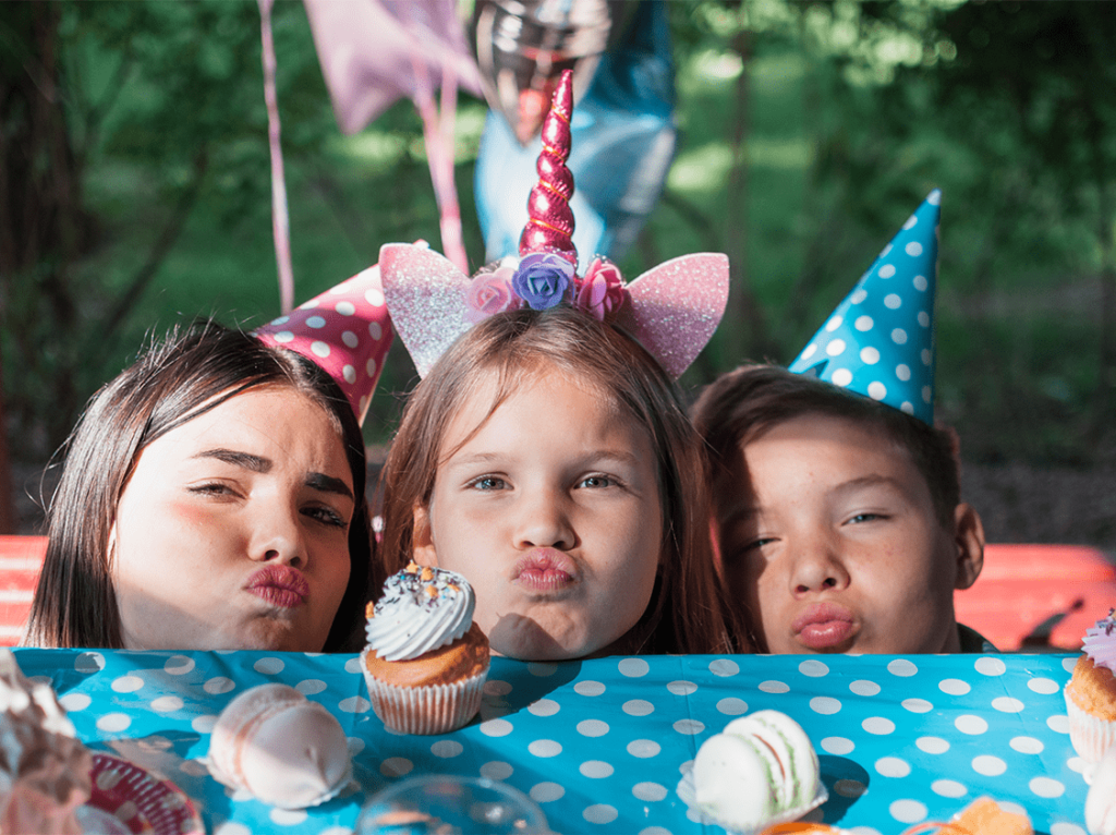 Kids wearing party hats and unicorn-themed accessories, enjoying cupcakes and desserts at a vibrant birthday party.